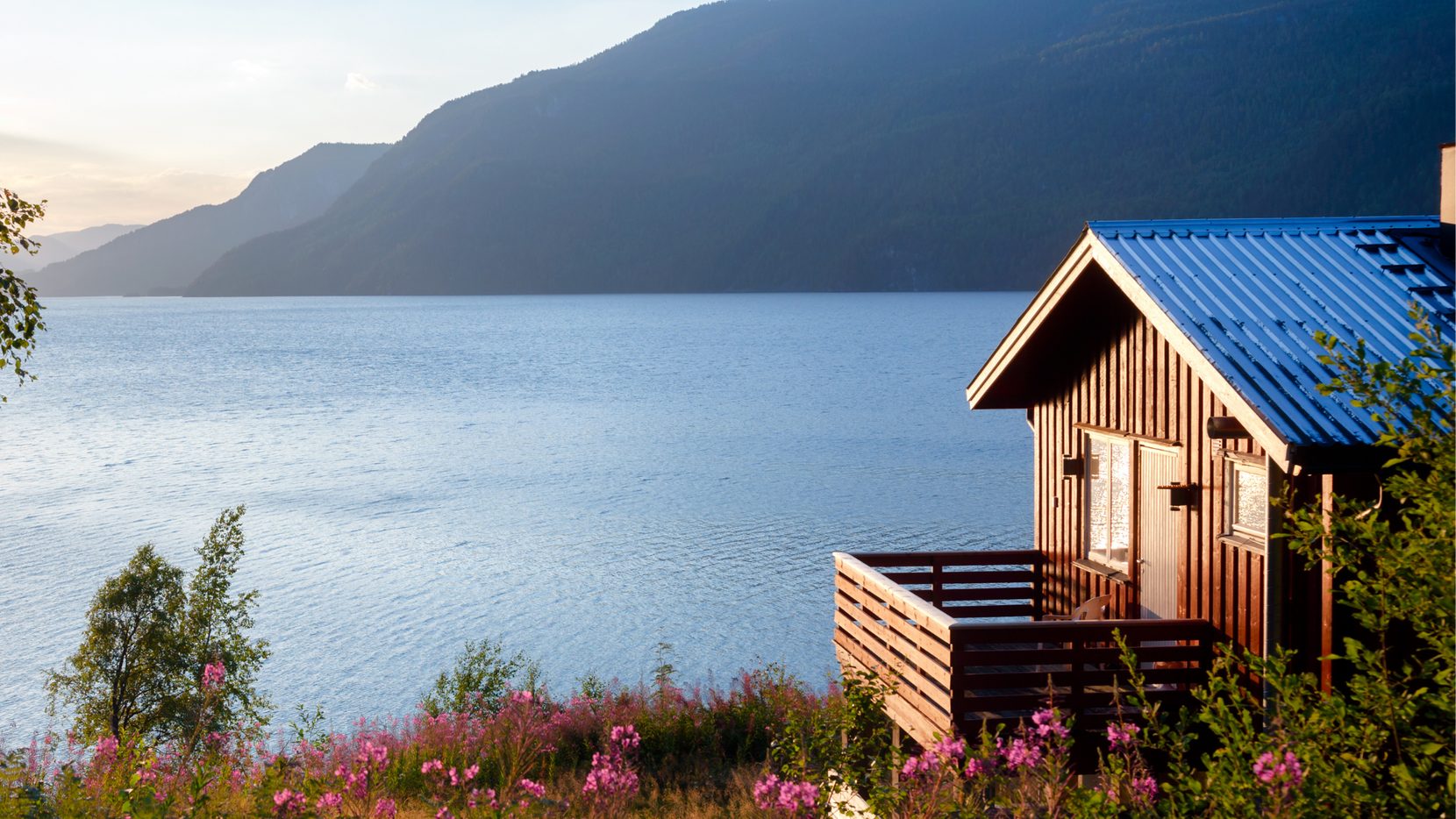 Casa modular em madeira com cobertura metálica, junto a um lago de montanha ao entardecer